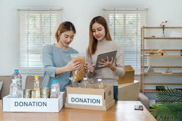 Two Women Organizing Donations in a Bright Room with Boxes and Supplies for Charity and Community...