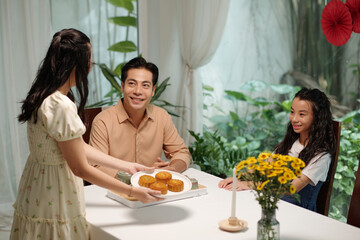 Woman serving baked cake for dessert while her family sitting at dining table