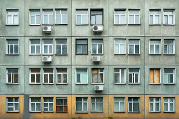 Naklejka premium Facade of an old multi-story residential building with uniform windows and some air conditioners. The building shows signs of wear and a lack of maintenance.