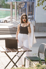 Stylish Businesswoman in Striped Pants and Sunglasses with Laptop Outdoors