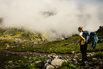 A Hiker is Adventurously Exploring a Lush Mountain Trail Surrounded by Misty Clouds