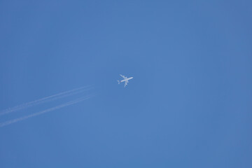 Large airliner in the blue sky without clouds. There is a clear line behind the plane