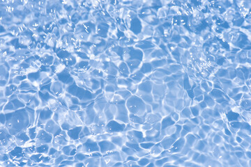 Blue water with ripples on the surface. Defocus blurred transparent blue colored clear calm water surface texture with splashes and bubbles. Water waves with shining pattern texture background.