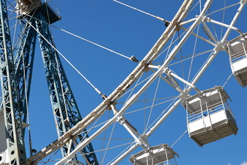 Detailed View Of A Ferris Wheel With Empty Cabins Set Against A Vibrant Blue Sky, Evoking A Sense Of Adventure And Nostalgia Associated With Amusement Parks.