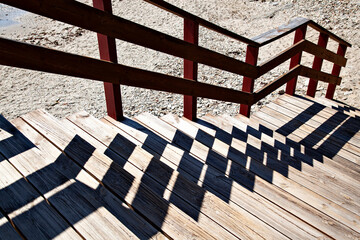 escalera de bajada a la playa  hecha de madera con escalones con sombras que hacen un dise&ntilde;o oscuro