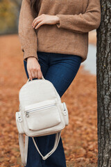 Close up fashion look details, modern autumn clothes, wear. Fall style for woman: white leather backpack, brown knitted sweater and jeans