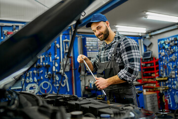 A proud Caucasian mechanic showcases workshop ownership, skillfully holding tools, capturing the essence of automotive expertise.