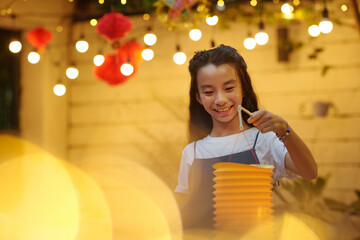 Happy Asian girl playing with lantern outdoors in decorated backyard © DragonImages