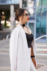 Stylish Young Woman in Striped Suit and Sunglasses with Urban Backdrop