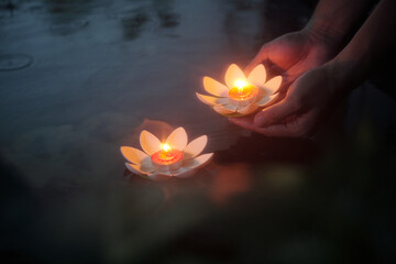 Close-up of woman putting candles in the shape of lilies on the water