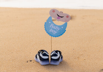 It's a boy and it's a girl baby written text announcement on the beach sand with shoe. Clean sea water and small beach waves are in background