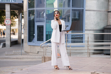 Confident Businesswoman in Chic Striped Suit Using Laptop Outdoors