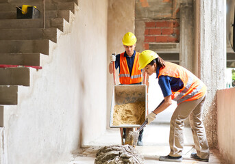 Young male and female masons working together while mixing cement at incomplete housing development