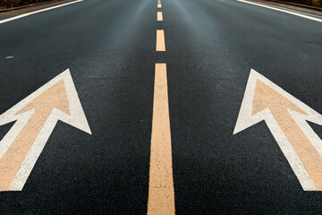 Close-up of a two-way asphalt road with double yellow lines and directional arrows indicating left and right lanes, symbolizing bidirectional traffic.