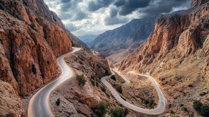 Wide shot of a mountainous road with hairpin turns, surrounded by dramatic rock formations and a cloudy sky