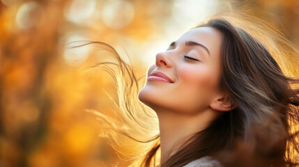 Naklejka premium A close-up of a smiling woman with her eyes closed, face lifted towards the sky, light wind gently lifting her hair.