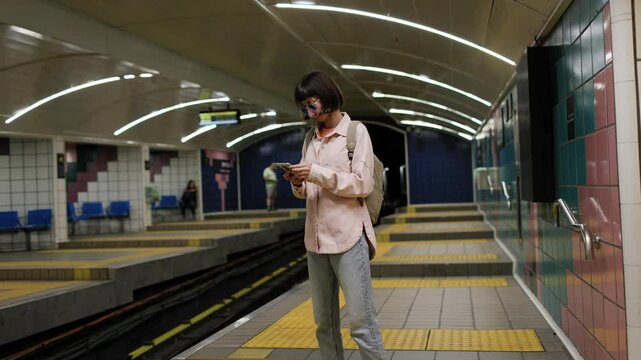girl waiting for train. girl in subway. Young girl in stylish clothes with backpack using smartphone in subway. fashion and style.