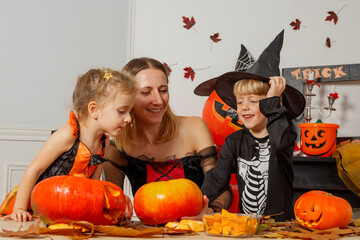Kids and mother laughing carving pumpkins in festive costumes