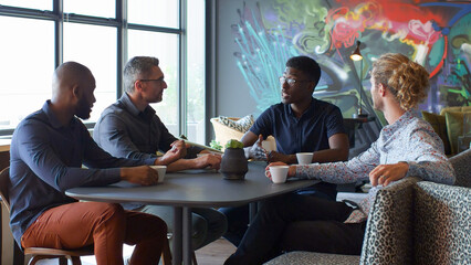 Multi-Cultural Male Business Team Around Table Having Informal Meeting In Modern Open Plan Office Together