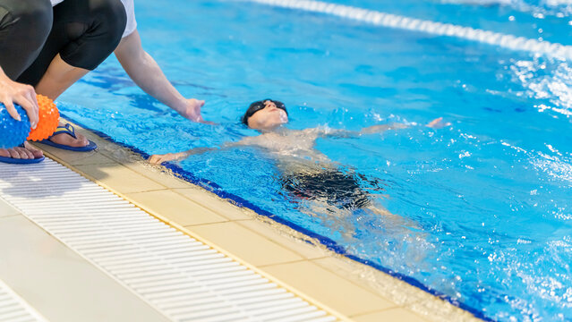 boy learning to swim in the pool with a trainer