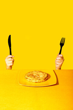 Hands holding a knife and fork over a meal against a yellow background