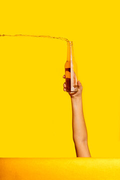 Hand holding a bottle with beer splashing against yellow background