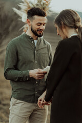 Groom reading vows holding bride's hands during outdoor wedding ceremony