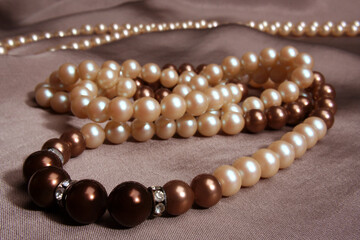 White and brown pearl necklace with diamond detail on a greyish fabric background
