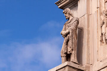 Fototapeta premium Side view of stone sculpture of bearded Roman with folded hands on blue sky background near Vatican, Rome