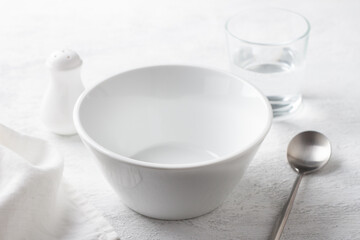 Simple table setting with white bowl, salt shaker, glass of water, and napkin on a gray surface