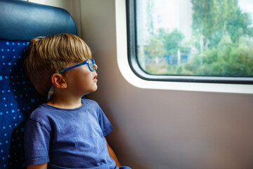 Young boy with glasses gazes out a train window, deep in thought