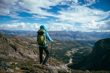 Backpacking woman climbing up on steep cliff edge at high altitude mountains top
