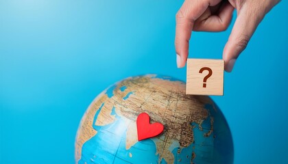 Hand hold wooden cube with question mark and red heart for questions on earth globe