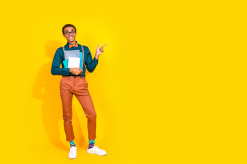 Full legnth photo of handsome young guy point empty space hold copybooks dressed stylish suit garment isolated on yellow color background