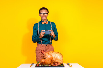 Portrait of elegant young man phone take picture roasted thanksgiving day turkey isolated on yellow...