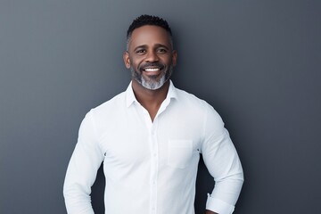 Smiling middle aged professional businessman looking at camera with natural posture. Happy mature man in his 40s wearing casual shirt, in sneakers standing isolated on gray background.