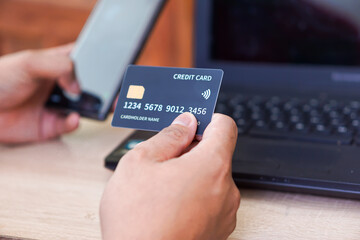 A person holding a credit card in one hand and a smartphone in the other while near a laptop.