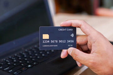A person holds a credit card in front of a laptop, indicating online transactions.