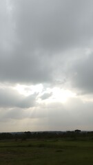 A gray, overcast sky with the sun just beginning to break through the clouds, casting beams of light onto the landscape below
