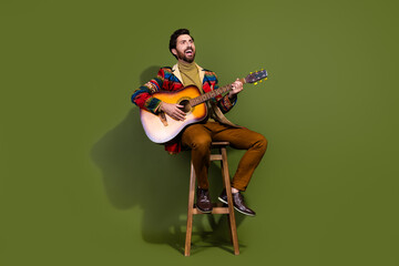Photo of nice cheerful man wear stylish clothes sit wooden stool play guitar empty space isolated...