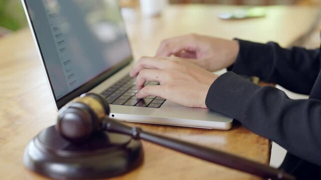 A person is using a laptop computer while a gavel is placed on the table in front of them. The person appears to be typing something important, perhaps a legal document or a report