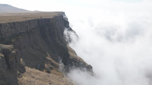 Thick, white clouds rise up rugged cliff face at edge of plateau atop Drakensberg mountains