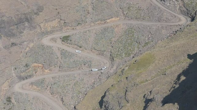 Wide aerial view of three offroad tour vehicles manoeuvring up the rugged Sani Pass