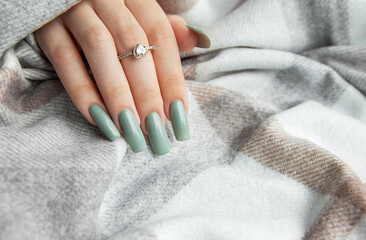 Elegant green nail polish on stylish long nails resting on a cozy blanket with a sparkly ring in soft indoor lighting