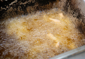 The frying oil sizzles as bubbles rise to the surface, turning the food a golden and crispy texture, highlighting the deep-fry cooking process in the hot kitchen. Junk food fat.