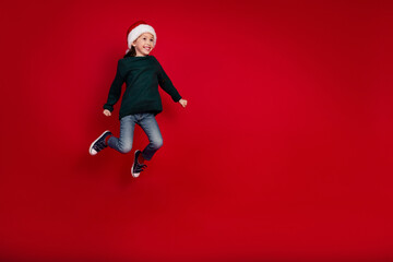 Full size photo of pretty small girl jumping have fun wear green christmas outfit theme party on red color background