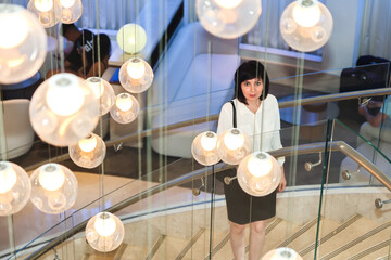 Elegant Brunette in Business Attire Ascending Grand Staircase Beneath Stunning Chandelier, Embodying Confidence and Professionalism in a Luxurious Setting.