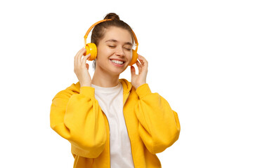Happy young woman in yellow hoodie smiling with closed eyes, enjoying music via wireless headphones