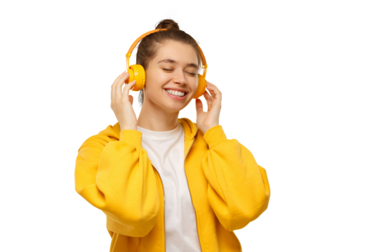 Happy young woman in yellow hoodie smiling with closed eyes, enjoying music via wireless headphones