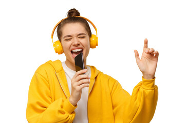 Young girl in yellow hoodie and wireless headphones, singing with closed eyes, holding smartphone as microphone